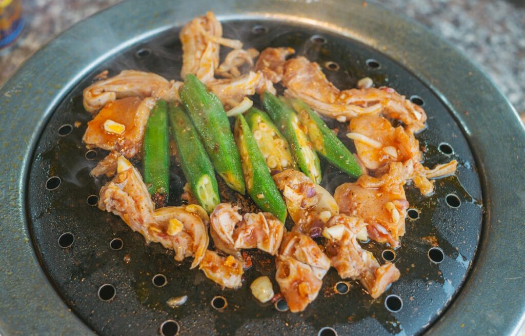 A close up of a grill with marinated meats and vegetables highlighting the sizzling action