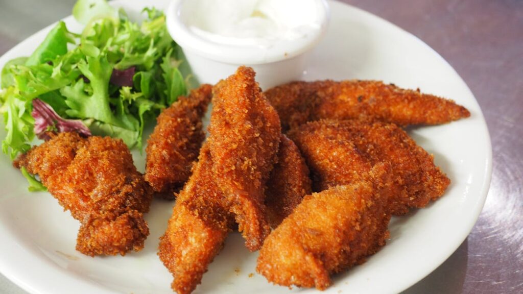 A plate of golden crispy chicken broast with a side of dipping sauce and a garnish of herbs