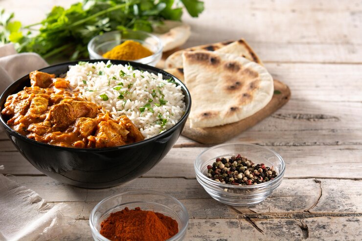 Chicken Tikka Masala in a bowl garnished with cilantro alongside a plate of naan or basmati rice